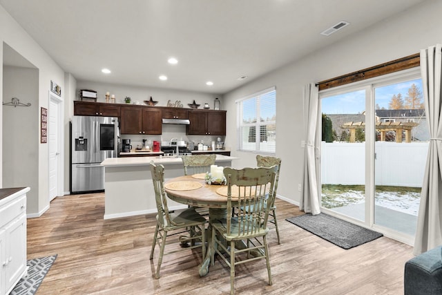 kitchen with a sink, under cabinet range hood, light wood-style flooring, light countertops, and appliances with stainless steel finishes