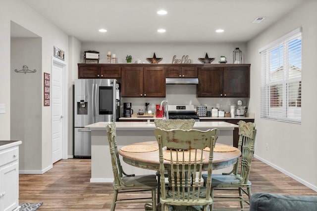 kitchen with a sink, visible vents, under cabinet range hood, light wood finished floors, and appliances with stainless steel finishes
