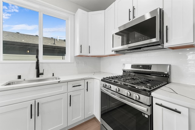 kitchen with white cabinetry, sink, decorative backsplash, light stone counters, and stainless steel appliances