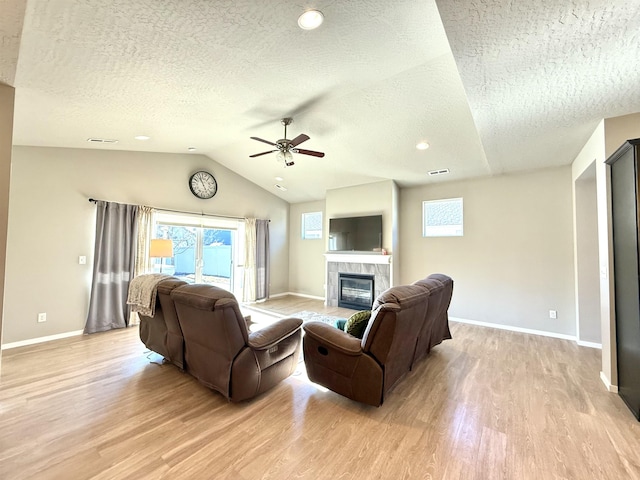 living room featuring vaulted ceiling, light hardwood / wood-style floors, a tile fireplace, and a textured ceiling