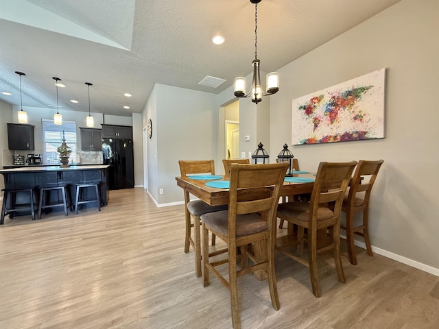 dining space featuring vaulted ceiling, a chandelier, light hardwood / wood-style floors, and a textured ceiling