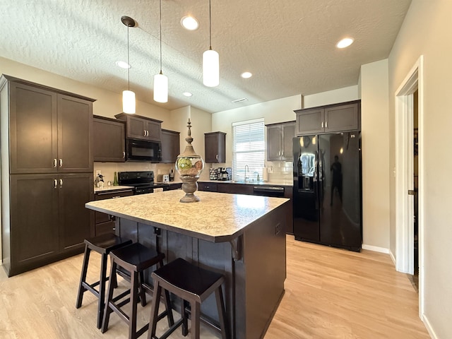 kitchen with sink, black appliances, a textured ceiling, a kitchen island, and decorative light fixtures