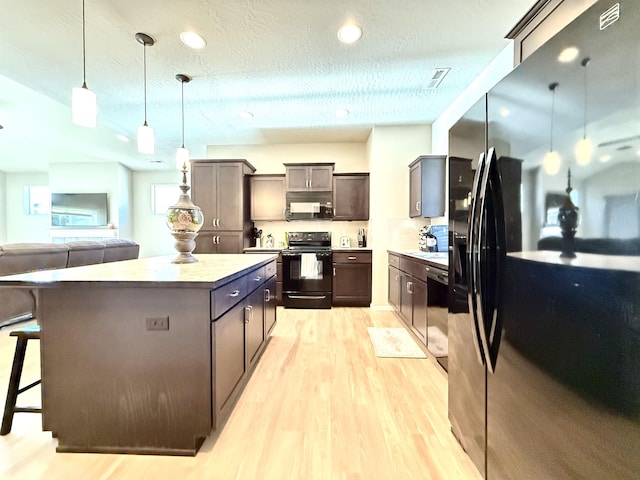 kitchen featuring pendant lighting, black appliances, light hardwood / wood-style floors, a textured ceiling, and a kitchen bar