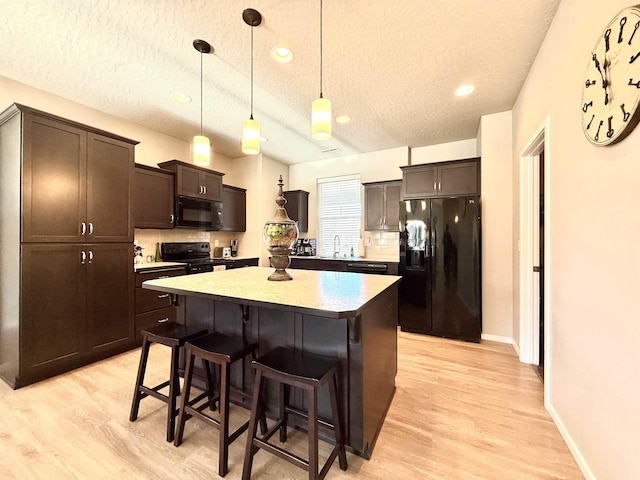 kitchen with a breakfast bar area, hanging light fixtures, black appliances, a textured ceiling, and a kitchen island