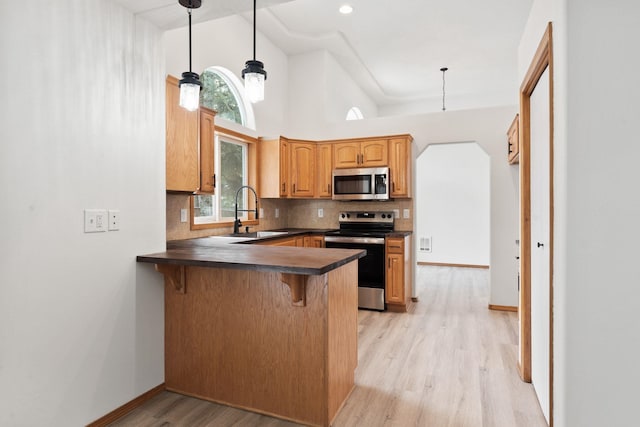 kitchen featuring a towering ceiling, decorative light fixtures, sink, kitchen peninsula, and stainless steel appliances