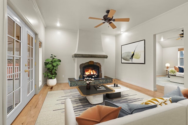 living room featuring crown molding, a large fireplace, ceiling fan, and light hardwood / wood-style floors