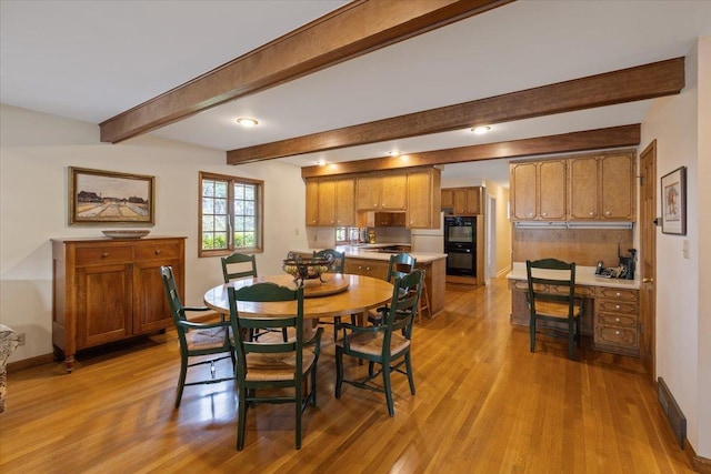 dining room with built in desk, beamed ceiling, and light wood-type flooring