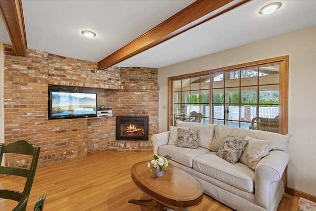 living room with beamed ceiling, brick wall, wood-type flooring, and a fireplace