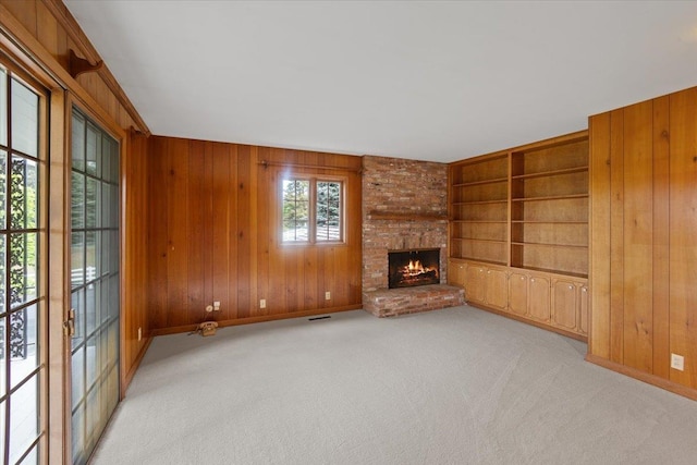 unfurnished living room featuring a brick fireplace, light carpet, built in features, and wooden walls