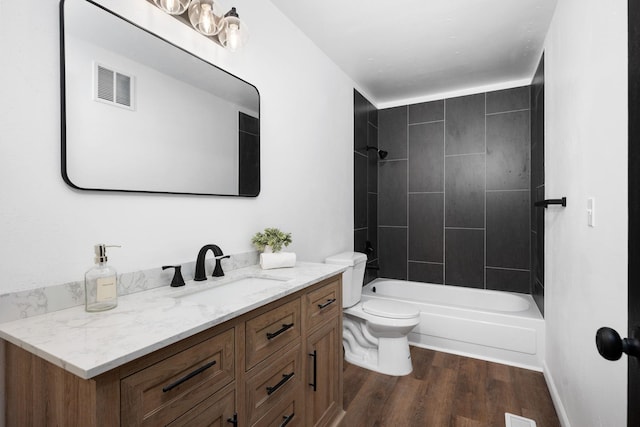 full bathroom with hardwood / wood-style flooring, vanity, tiled shower / bath, and toilet