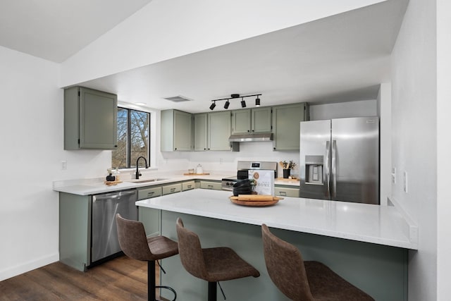 kitchen with sink, green cabinets, stainless steel appliances, dark hardwood / wood-style floors, and a kitchen bar