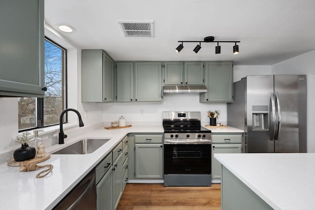 kitchen with rail lighting, sink, stainless steel appliances, light stone countertops, and light wood-type flooring