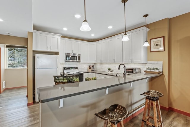 kitchen featuring white refrigerator, electric range oven, kitchen peninsula, and a breakfast bar