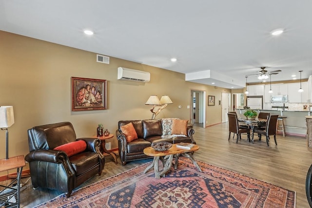 living room featuring an AC wall unit, hardwood / wood-style floors, and ceiling fan