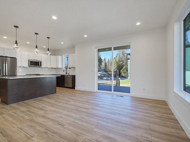 kitchen featuring pendant lighting, white cabinetry, stainless steel appliances, light hardwood / wood-style floors, and a kitchen island