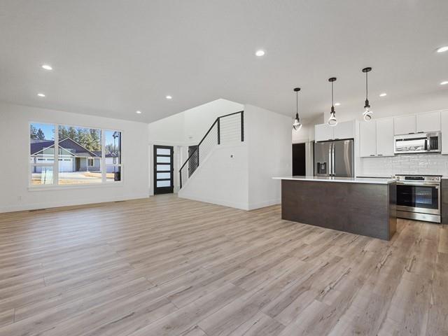 kitchen featuring a center island, hanging light fixtures, white cabinets, stainless steel appliances, and backsplash