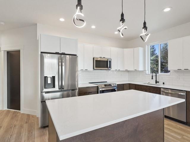 kitchen featuring sink, appliances with stainless steel finishes, white cabinetry, a kitchen island, and decorative light fixtures