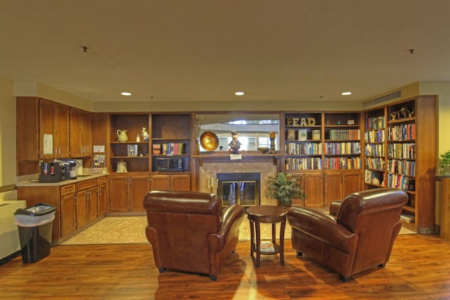 living room featuring a tiled fireplace, built in shelves, and light hardwood / wood-style flooring