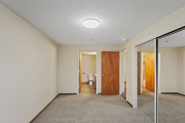 unfurnished bedroom with light carpet, a textured ceiling, ensuite bath, and a closet