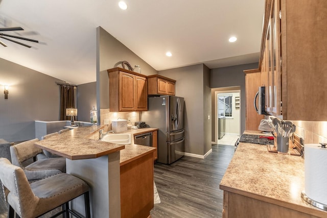 kitchen with sink, dark wood-type flooring, a breakfast bar, stainless steel appliances, and kitchen peninsula