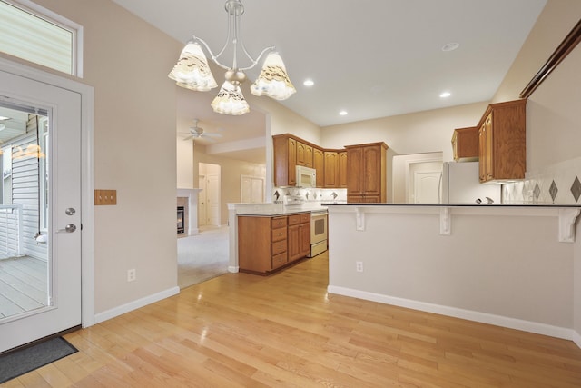 kitchen with white appliances, hanging light fixtures, a kitchen bar, kitchen peninsula, and light wood-type flooring