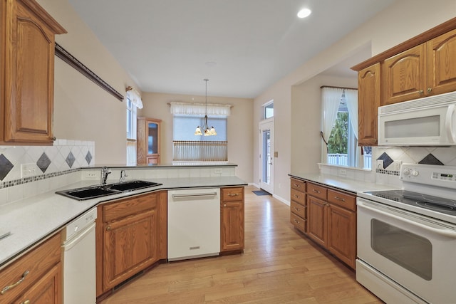 kitchen featuring sink, light wood-type flooring, hanging light fixtures, white appliances, and an inviting chandelier