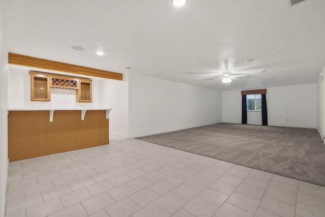 carpeted empty room featuring ceiling fan and bar area