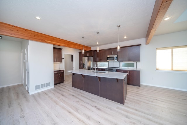 kitchen featuring appliances with stainless steel finishes, pendant lighting, beamed ceiling, an island with sink, and dark brown cabinets