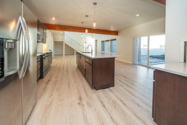 kitchen with decorative light fixtures, beamed ceiling, sink, stainless steel appliances, and a center island with sink