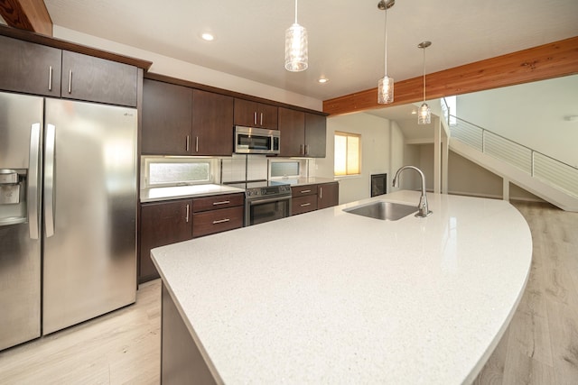 kitchen featuring an island with sink, sink, hanging light fixtures, stainless steel appliances, and beam ceiling