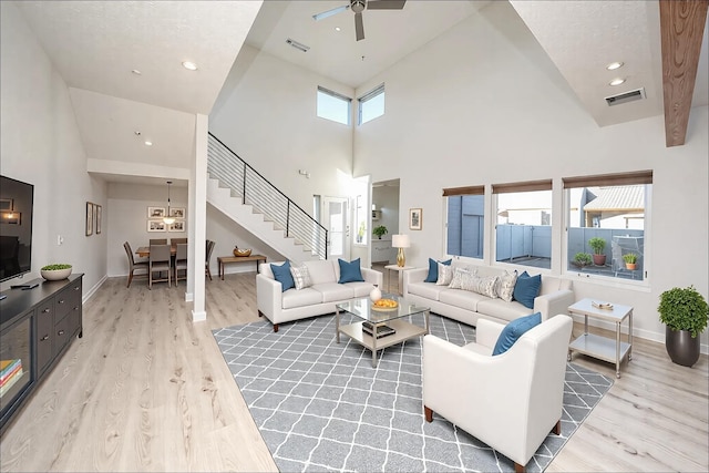 living room featuring ceiling fan, a towering ceiling, and light wood-type flooring