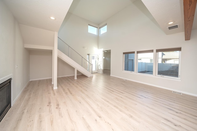 unfurnished living room featuring light wood-type flooring, a healthy amount of sunlight, and a high ceiling