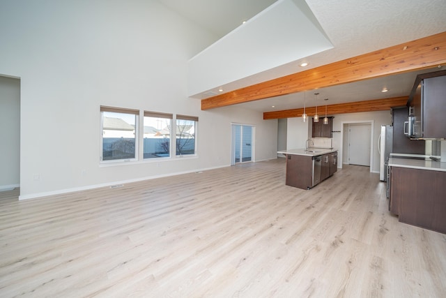 kitchen with sink, light hardwood / wood-style flooring, appliances with stainless steel finishes, pendant lighting, and a kitchen island with sink