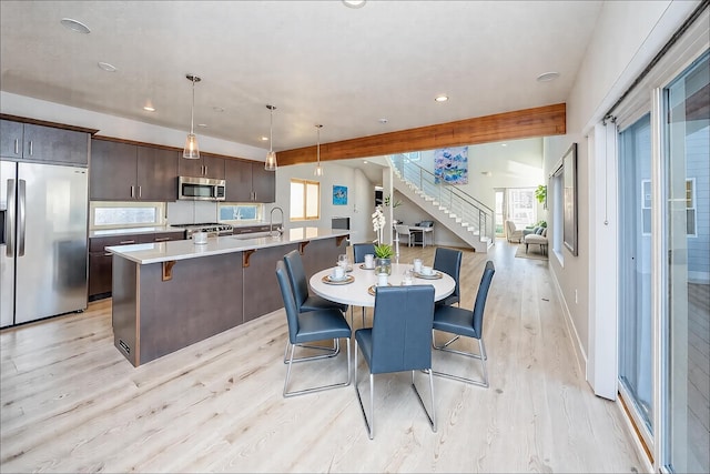 dining space with light wood-type flooring, sink, and beam ceiling