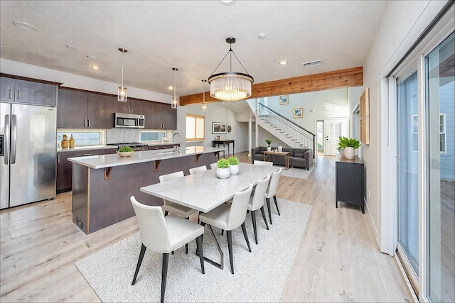 dining space featuring beamed ceiling, a healthy amount of sunlight, sink, and light hardwood / wood-style floors