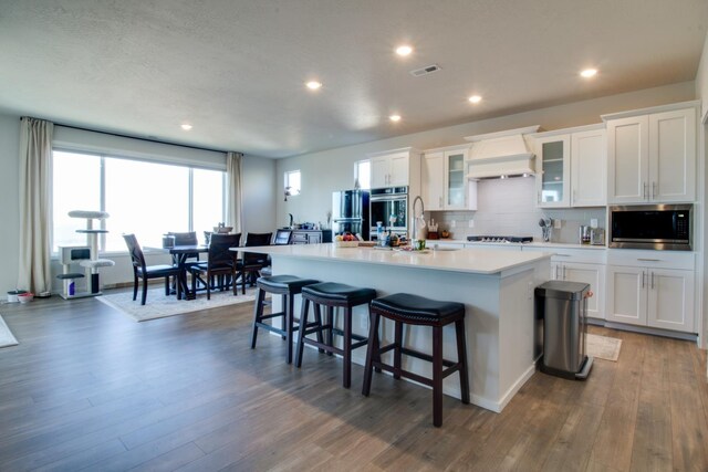 kitchen featuring appliances with stainless steel finishes, dark hardwood / wood-style floors, an island with sink, white cabinets, and a kitchen bar