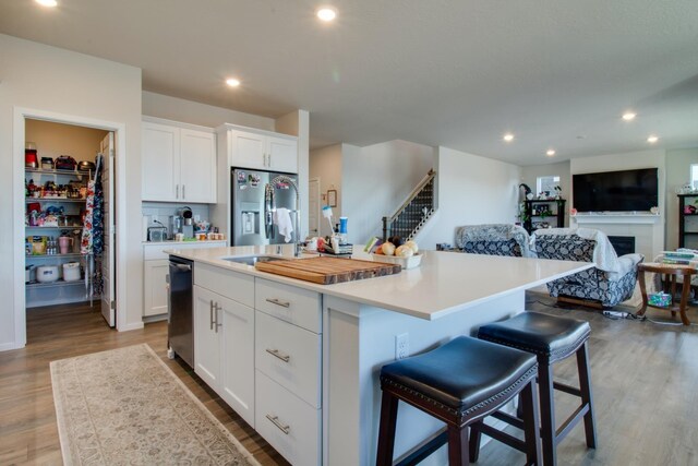 kitchen with a breakfast bar area, light wood-type flooring, an island with sink, stainless steel appliances, and white cabinets