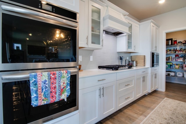 kitchen with light hardwood / wood-style flooring, white cabinetry, backsplash, stainless steel appliances, and custom exhaust hood