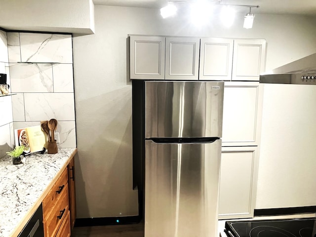 kitchen featuring white cabinetry, stainless steel fridge, light stone counters, and wall chimney exhaust hood