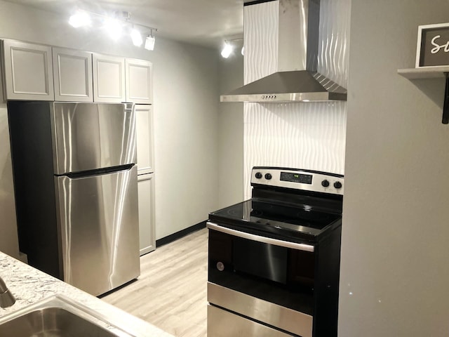 kitchen with appliances with stainless steel finishes, white cabinetry, light stone counters, wall chimney exhaust hood, and light wood-type flooring