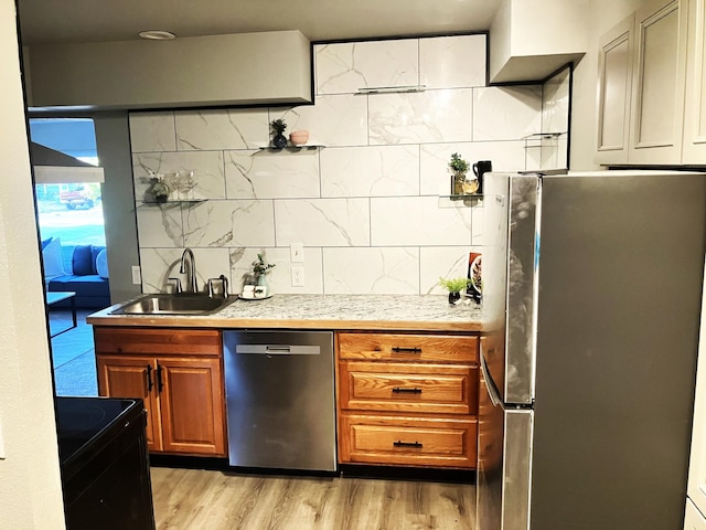 kitchen with tasteful backsplash, appliances with stainless steel finishes, sink, and light wood-type flooring