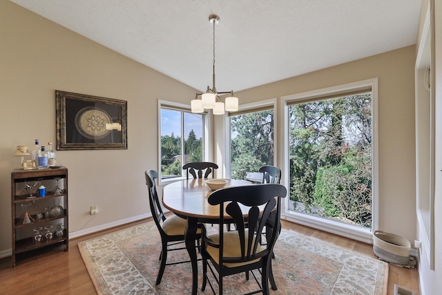 dining room with hardwood / wood-style flooring, vaulted ceiling, and a chandelier