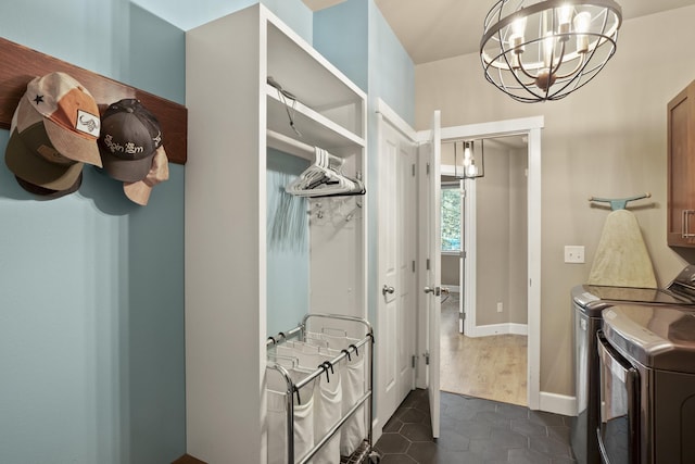clothes washing area featuring baseboards, dark tile patterned flooring, washer and dryer, cabinet space, and a notable chandelier