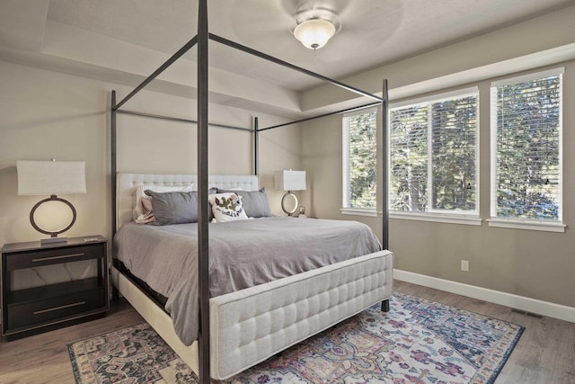 bedroom featuring baseboards, visible vents, wood finished floors, and multiple windows