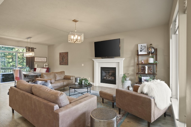 living room with a notable chandelier, a glass covered fireplace, and wood finished floors