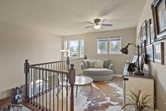 living area with a textured ceiling, wood finished floors, an upstairs landing, and baseboards