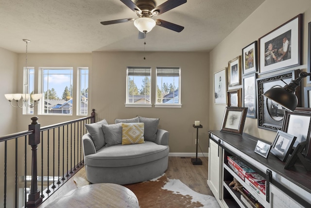living area featuring light wood finished floors, baseboards, ceiling fan, and a textured ceiling