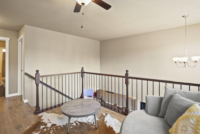 living area with ceiling fan with notable chandelier, baseboards, wood finished floors, and an upstairs landing