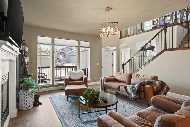 living room featuring light wood finished floors, stairway, a chandelier, a tile fireplace, and baseboards