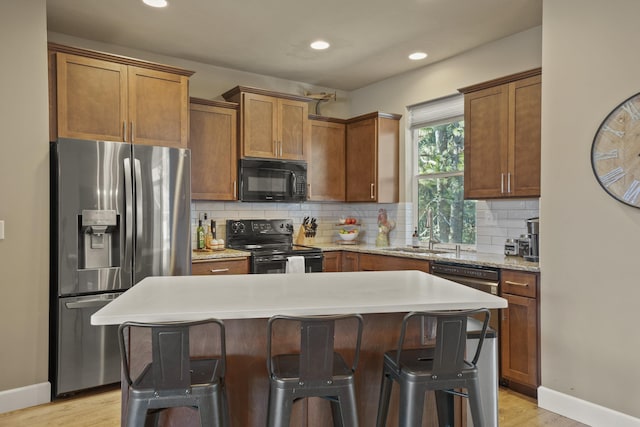 kitchen with light wood-style flooring, backsplash, a sink, black appliances, and a kitchen breakfast bar